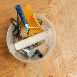 A collection of home renovation tools in a bucket on a wooden floor, ready for a painting project. — Is Texas a Good Place to
