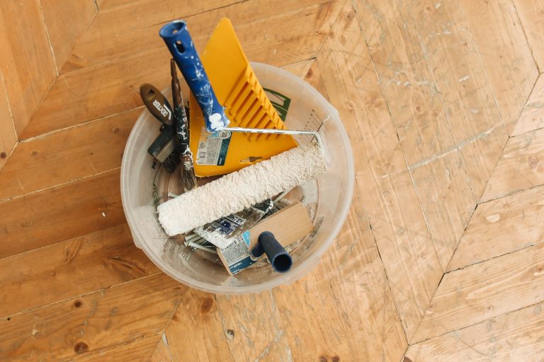 A collection of home renovation tools in a bucket on a wooden floor, ready for a painting project. — Is Texas a Good Place to