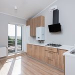 Stylish empty kitchen with wooden cabinets and large windows. — Risks of Asbestos in Attic Insulation